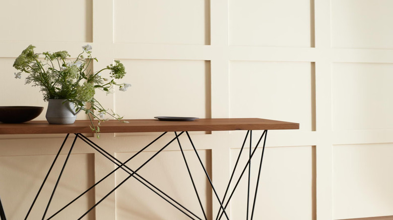 Flowering plant in white vase on top of wood table against cream colored wall