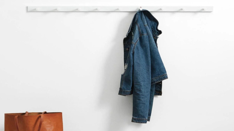 White wall with white coat rack with denim jacket hung on one hook