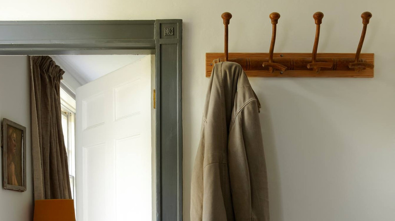 Wooden coat hanger on off white wall next to dark green door frame