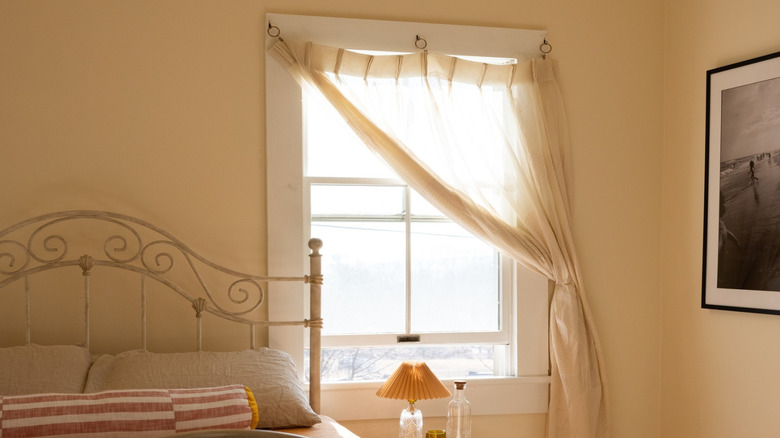 White window with beige gauze curtain on cream colored wall