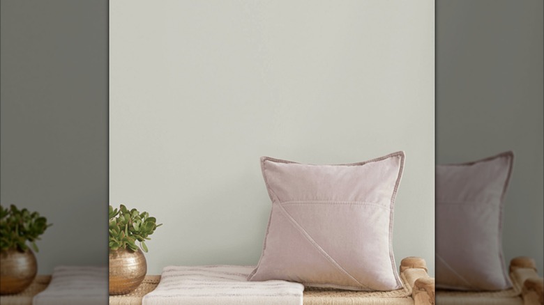Muted pink pillow and plant in bronze pot against greenish white wall