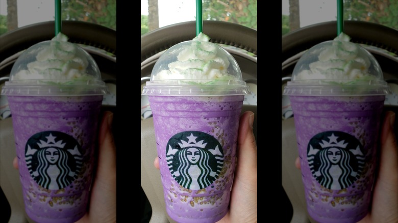 Mirrored image of hand holding Witch's Brew Crème Frappuccino in front of steering wheel