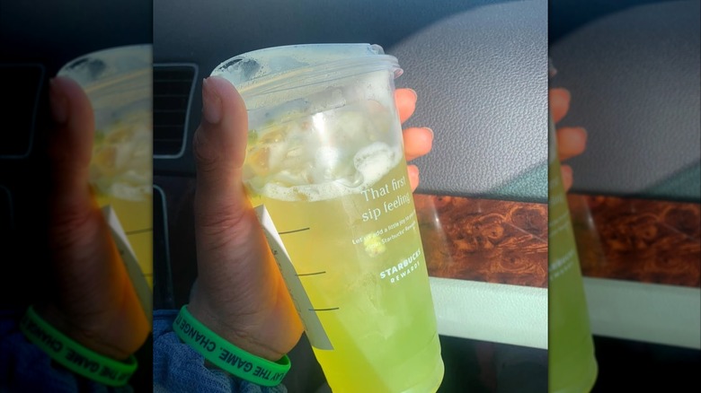 hand holding Kiwi Star Fruit Refresher from Starbucks with car interior in background