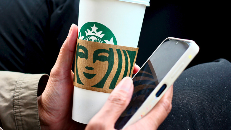 Hand holding Starbucks cup and using smartphone simultaneously
