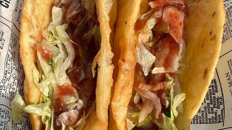 Two dill pickle cheese curd tacos on newspaper-style wrap.