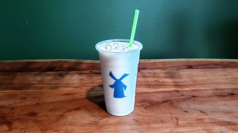 The vanilla shake from Dutch Bros in a plastic cup with a straw on a wooden counter