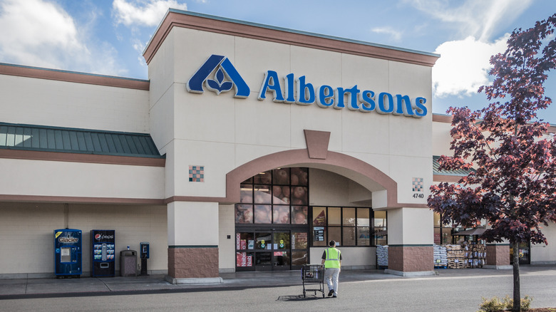 An employee in a yellow vest pushing a cart into an Albertsons grocery store.
