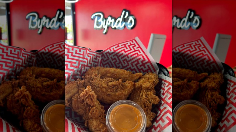 Hand holding container of chicken tenders with Byrd's Hot Chicken sign in background