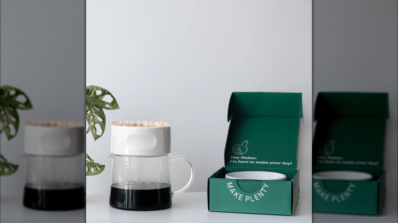 The Etkin 8-Cup Dripper on a glass carafe next to its box on a grey background