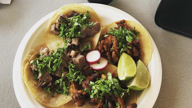Four street tacos on a white plate
