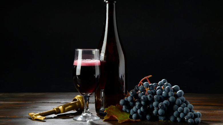 sparkling red wine bottle with glass and grapes on black background