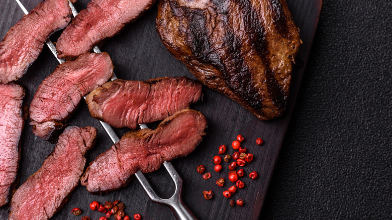 freshly cooked sliced steak on a dark board with red peppercorns
