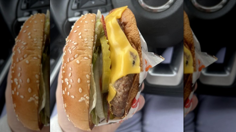 Mirrored image of hand holding Whopper in front of Nissan steering wheel