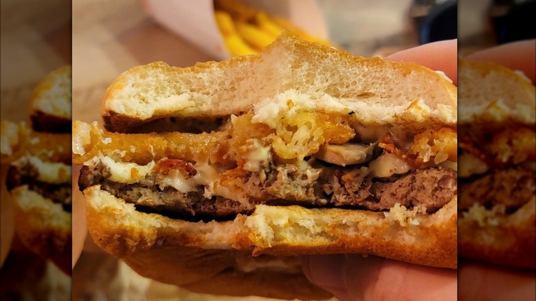 Mirrored image of hand holding half eaten Burger King Steakhouse Bacon Whopper