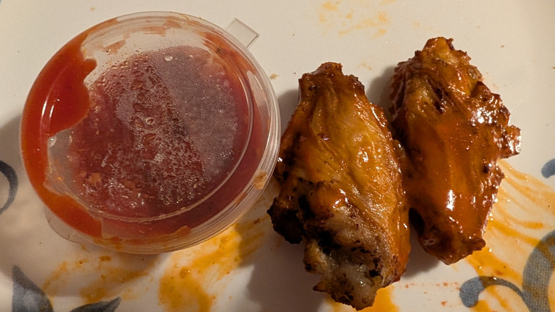 Two chicken wings next to sauce pot on patterned plate, close up