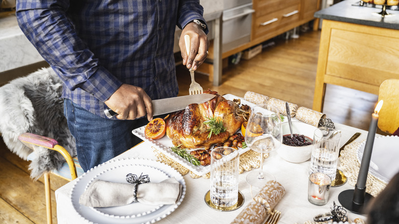 Hands carving a roast turkey on a square white platter