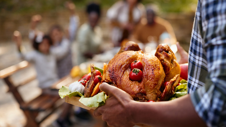 Hands carrying a turkey to the dinner table, with blurred people in the background