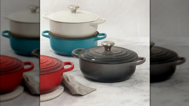 Multiple colors of lidded Le Creuset Sauteuse pans on marble countertop