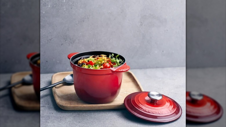 Red Le Creuset rice pot with lid taken off, sitting on wooden tray