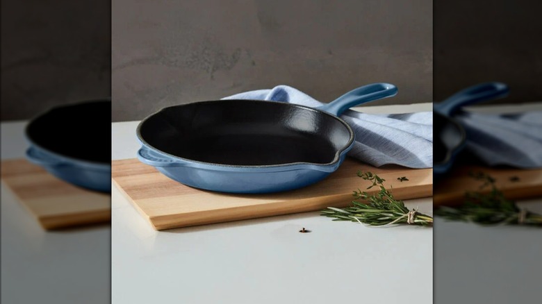 Blue Le Creuset skillet on wooden board on kitchen countertop