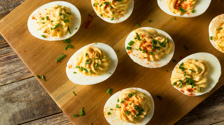 Deviled eggs with chives and paprika plated on a wooden board
