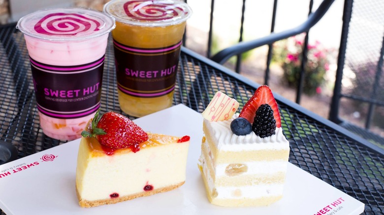 Two berry-topped slices of cake on table with two cups of bubble tea