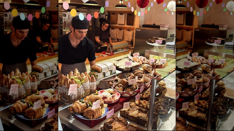 Baker standing behind display of cakes, pastries, and sandwiches on bakery counter