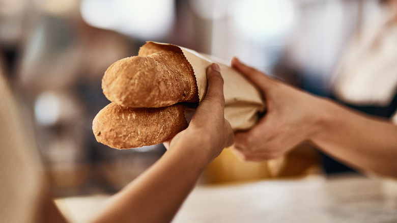 Bakery worker handing crusty loaves of bread to customer