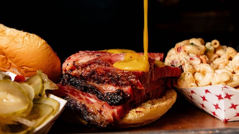 Sauce being drizzled on brisket with sides of mac and cheese, pickles, and bread at Green Street Smoked Meats