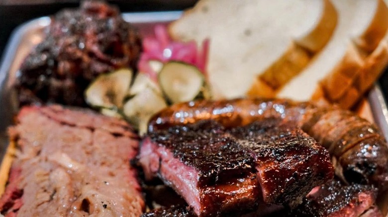 Close-up of BBQ platter with ribs, brisket, sausage, bread, and pickled sides