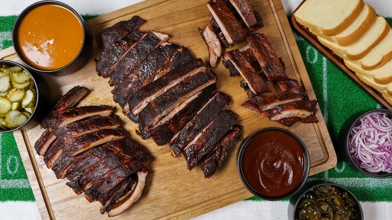 Top view of a wooden board with ribs, sauces, sides, and slices of bread at Smoque BBQ