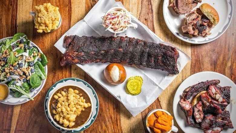 Wooden table with assortment of BBQ dishes including ribs, sandwiches, and sides