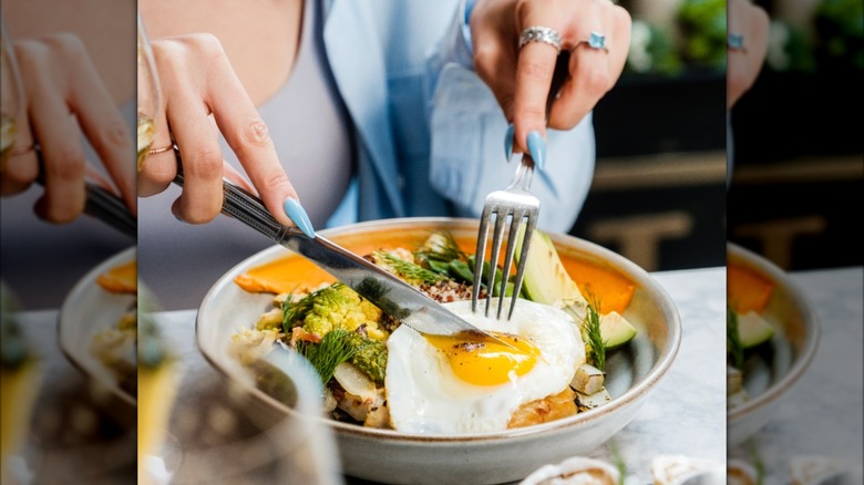 Cutting an egg on top of a breakfast bowl