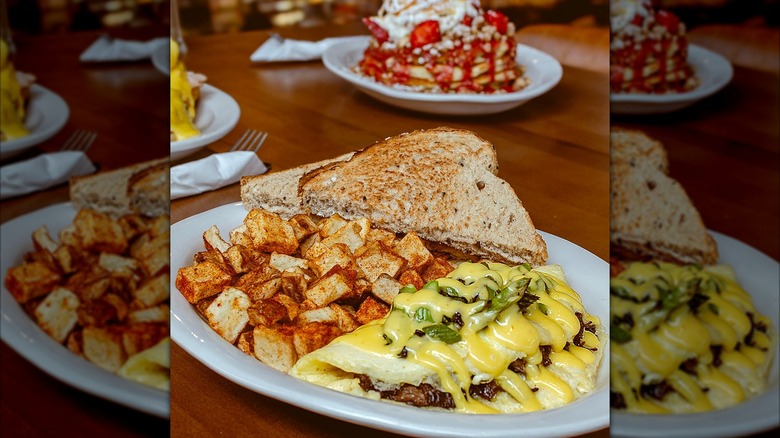 Toast, omelet, and homefries on a plate, with a plate of waffles and strawberries in blurred background