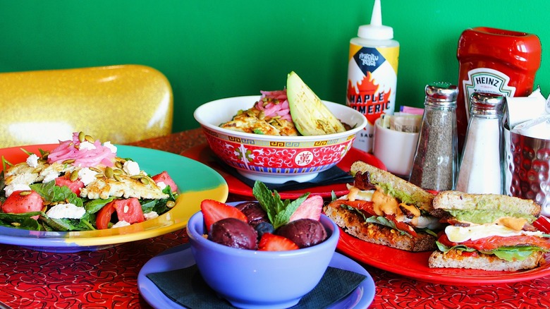 Brightly-colored table and dishes with salads, fruits, and breakfast sandwiches