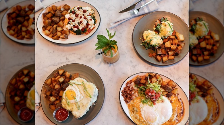 Four brunch dishes on a table from above with eggs Benedict and homefries