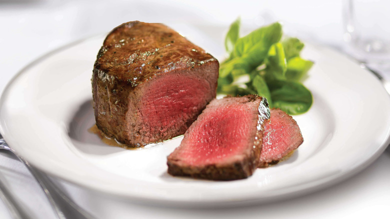 A medium rare filet mignon on an elegant white plate and table