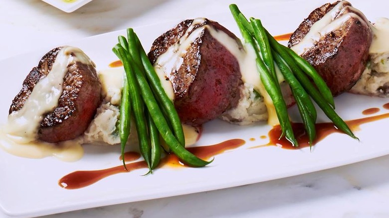 Three filets on a plate with sauce on top, green beans and mashed potatoes