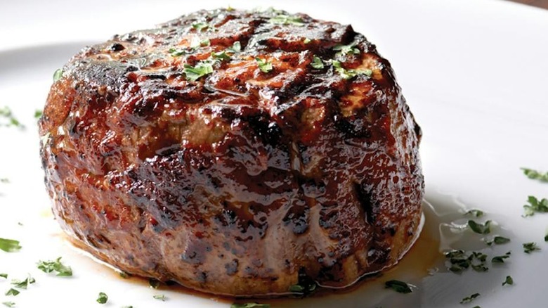 A juicy filet mignon on a white plate sprinkled with herbs