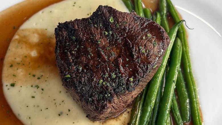 Cooked filet mignon on plate with sauce and green beans
