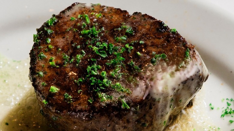 Cooked filet mignon on a white plate with herbs and butter