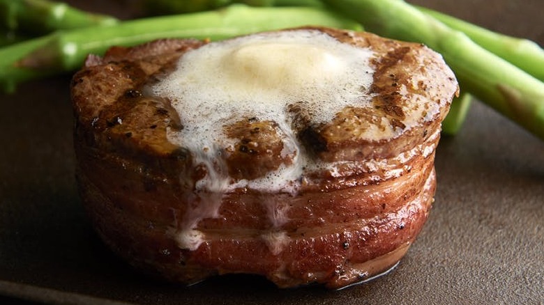 Filet mignon wrapped in bacon and topped with butter, asparagus on the side