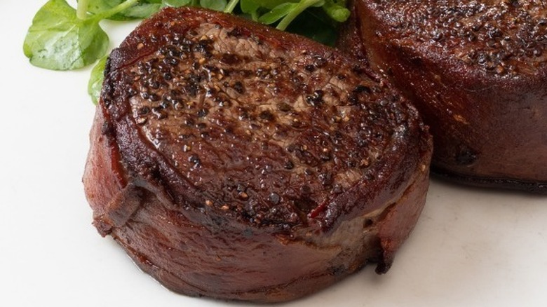 Two filet mignons next to each other on a white plate with a green garnish