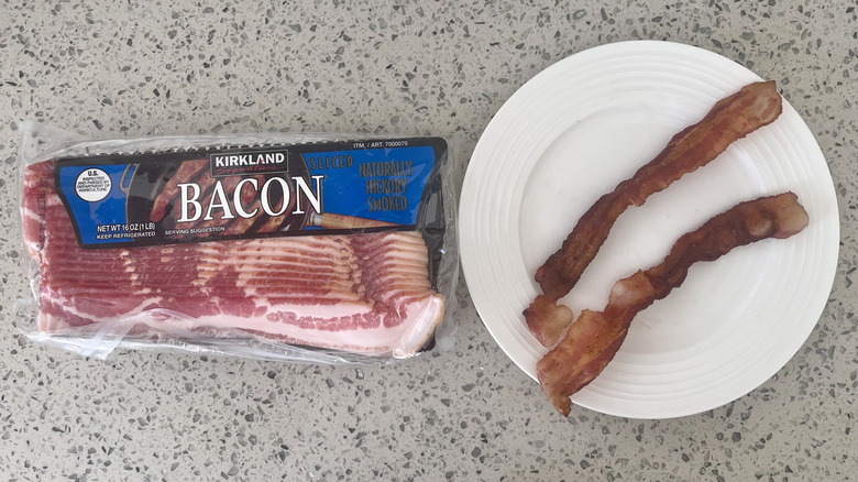 two slices of cooked bacon on a plate beside a package of Kirkland Signature Sliced Bacon