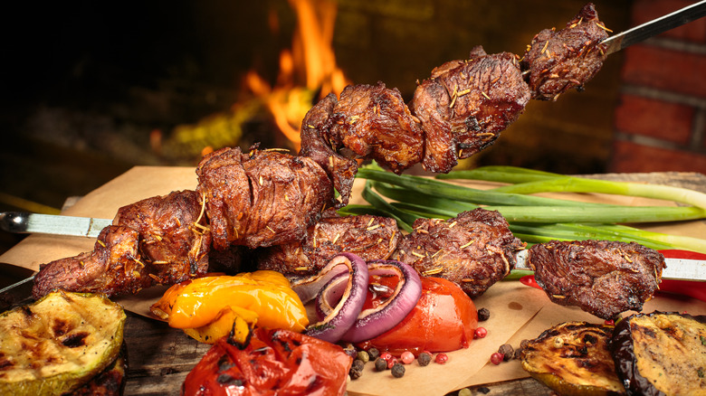 Marinated barbecue meat on skewer. Shish kebab or Shashlyk meaning skewered  meat. Beef or pork on grill on an open fire with smoke. Street food, picnic  concept Stock Photo