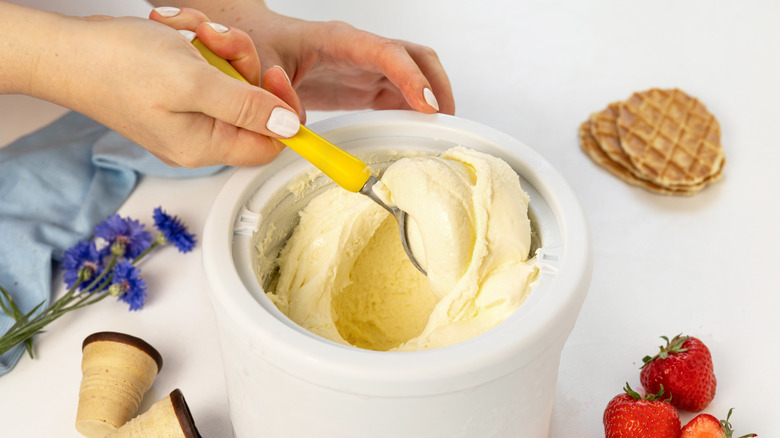 hands scooping vanilla ice cream out of a homemade ice cream churner