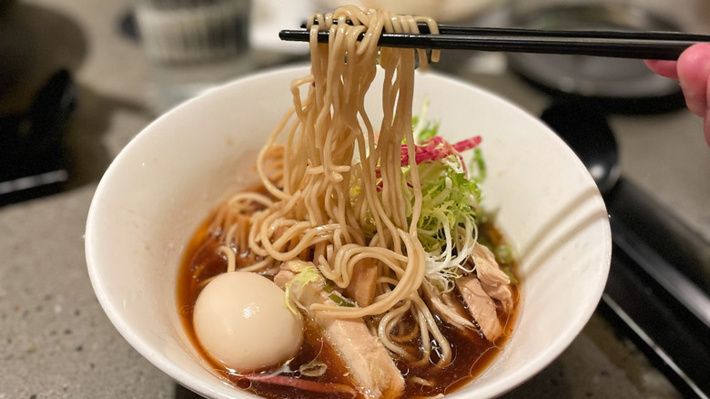 A person pulling ramen noodles from a bowl with chicken breast and poached egg at Whisky & Ramen