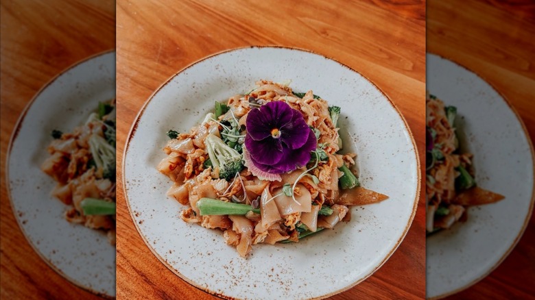 Pad see ew with wide rice noodles, vegetables, and edible flowers at Bodhi in Indianapolis