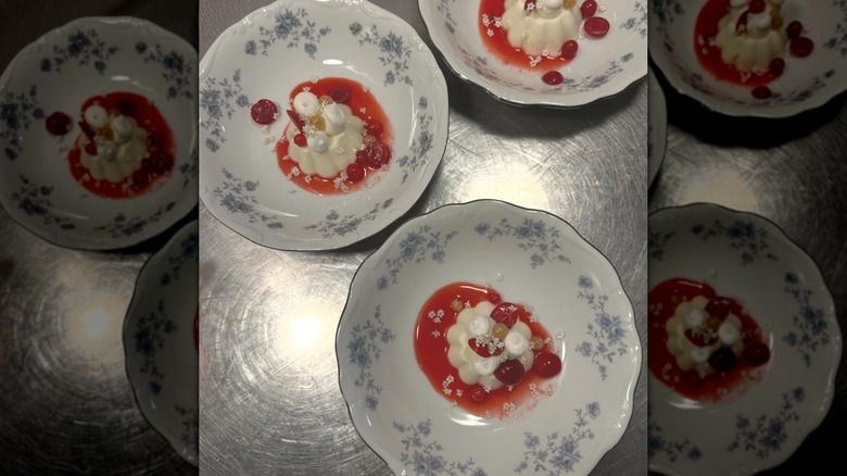 Pannacotta desserts served in floral plates with red fruit and sauce, all garnished with flowers