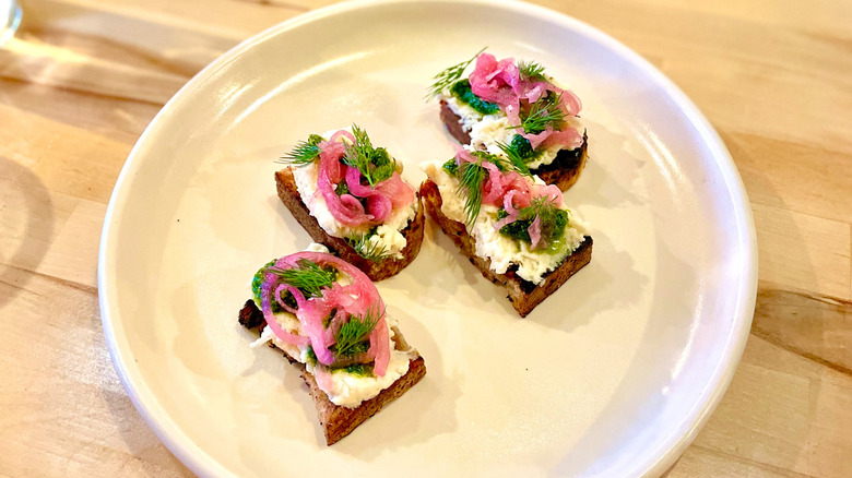 Sourdough crostini with sweet cream butter, herbs, and pickled onions served on a white plate at FarmBar in Tulsa